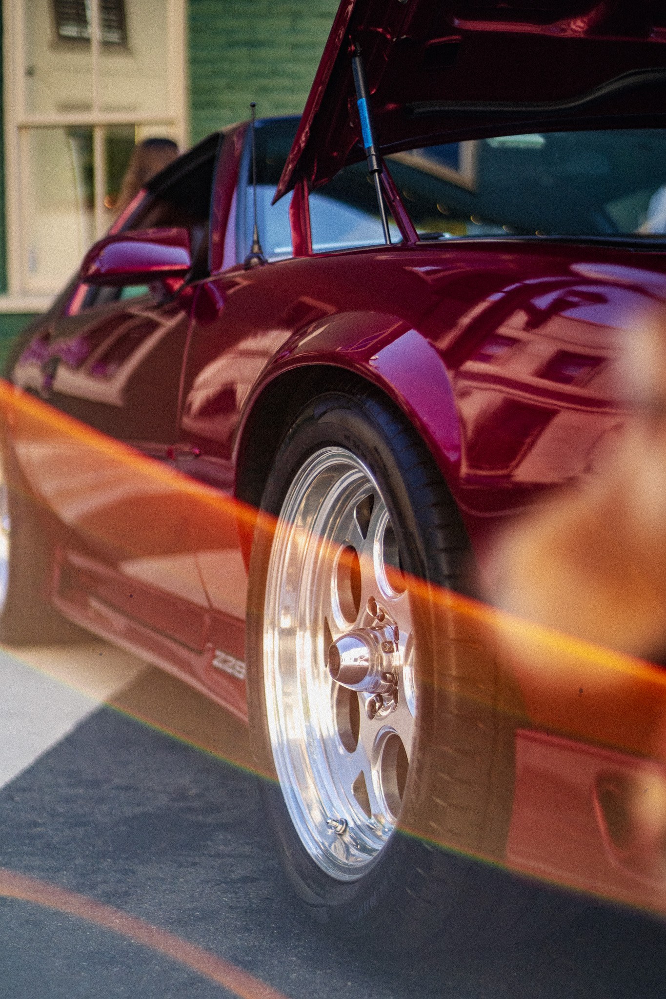 A red classic sports car with a polished wheel and a warm lens flare.