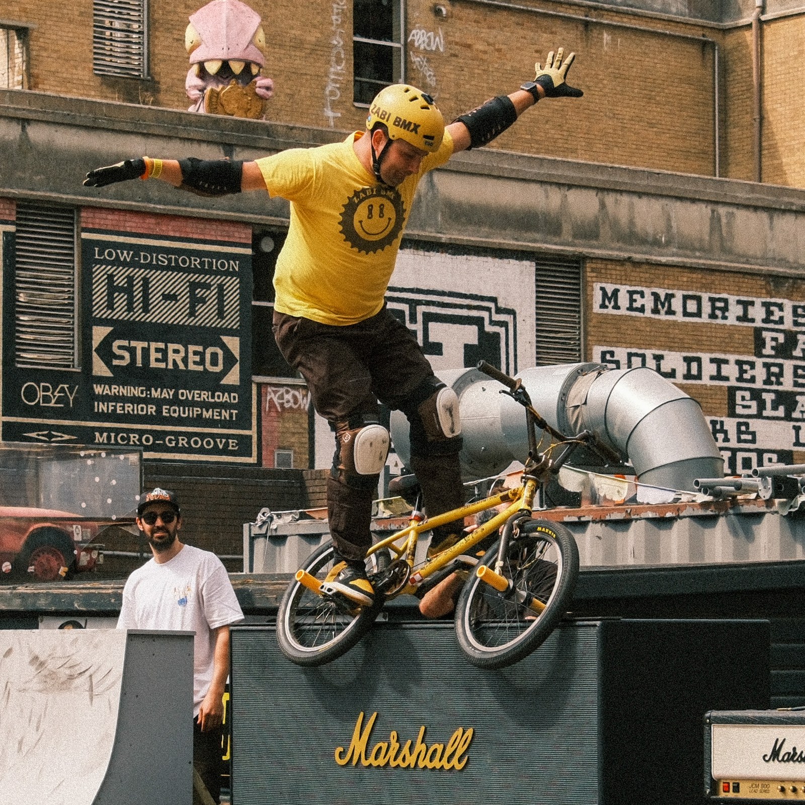 A BMX rider in a yellow shirt airborne above a ramp with arms extended.